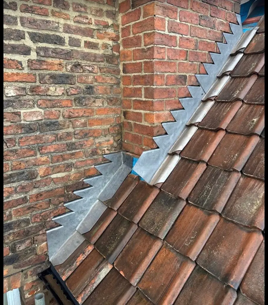 Lead step flashing cut and dressed into a brick chimney on a clay tile roof