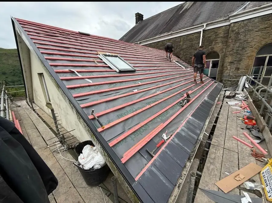 Roofers battening a re-roof around a new roof window over red membrane