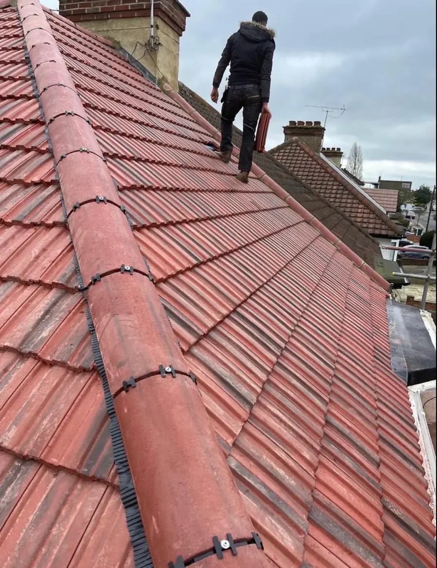 The same red tile roof with the dry ridge fitted, roofer walking the slope