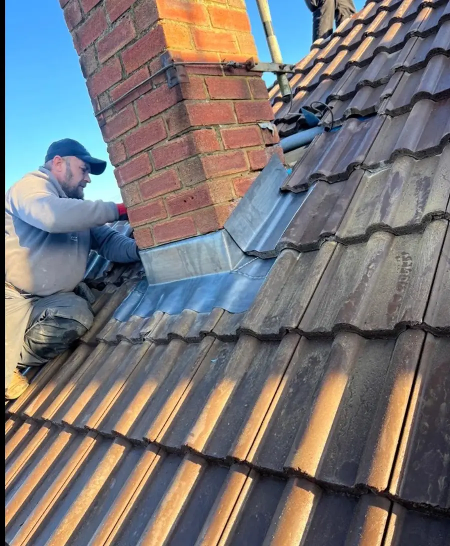 Roofer dressing new lead flashing around a brick chimney on a concrete tile roof