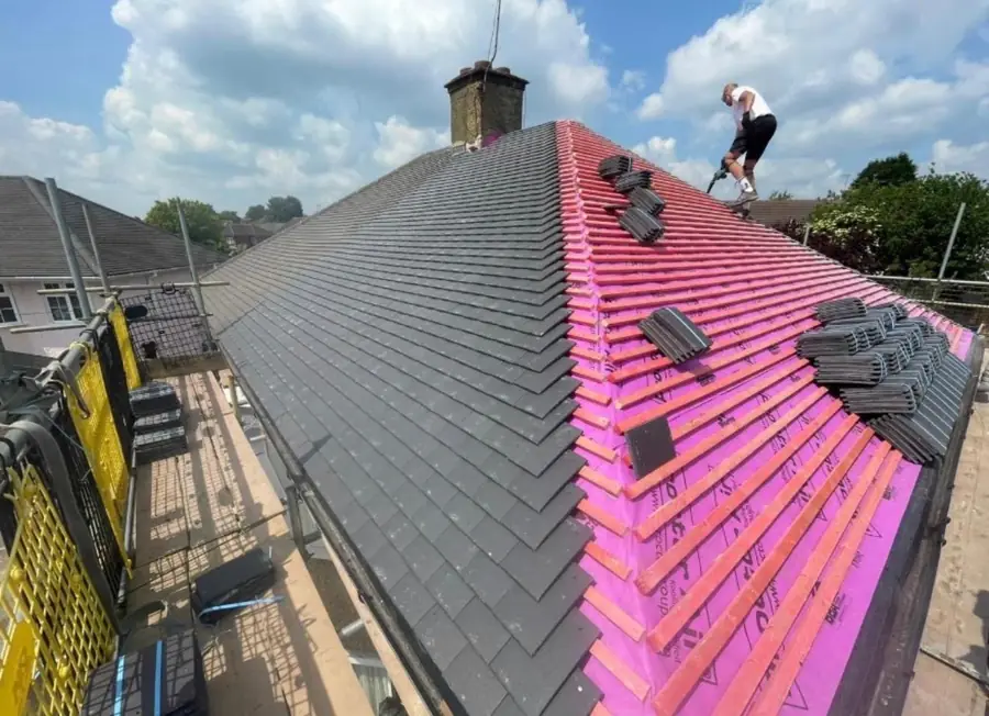 Slate-effect tiles going on over pink breathable membrane, roofer at the ridge