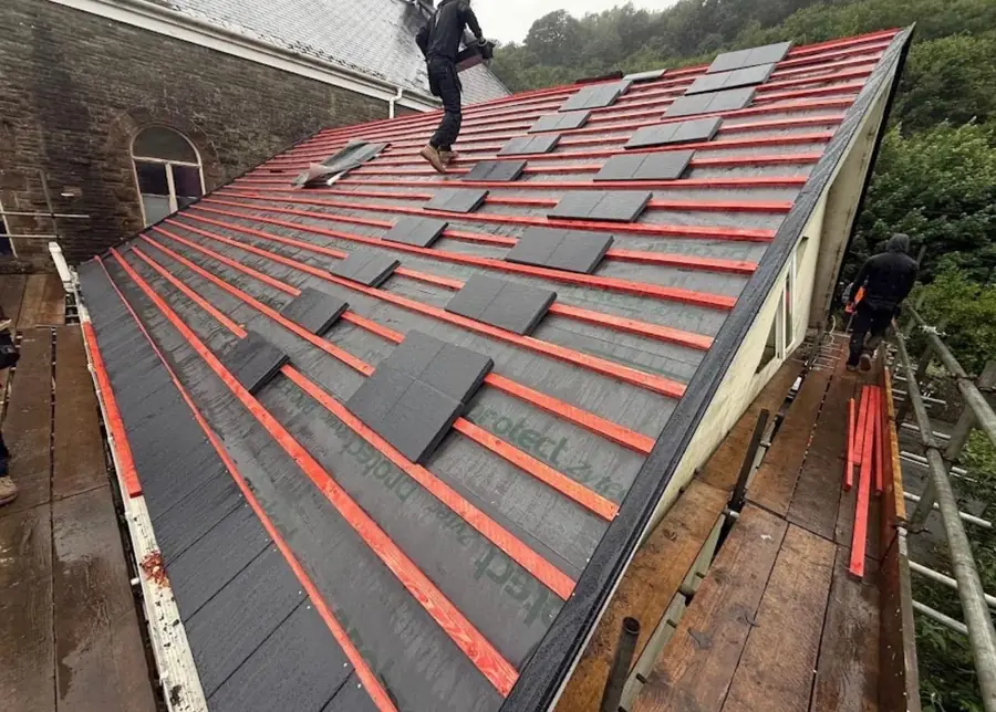 Team laying slate-effect tiles over red membrane on a long roof slope